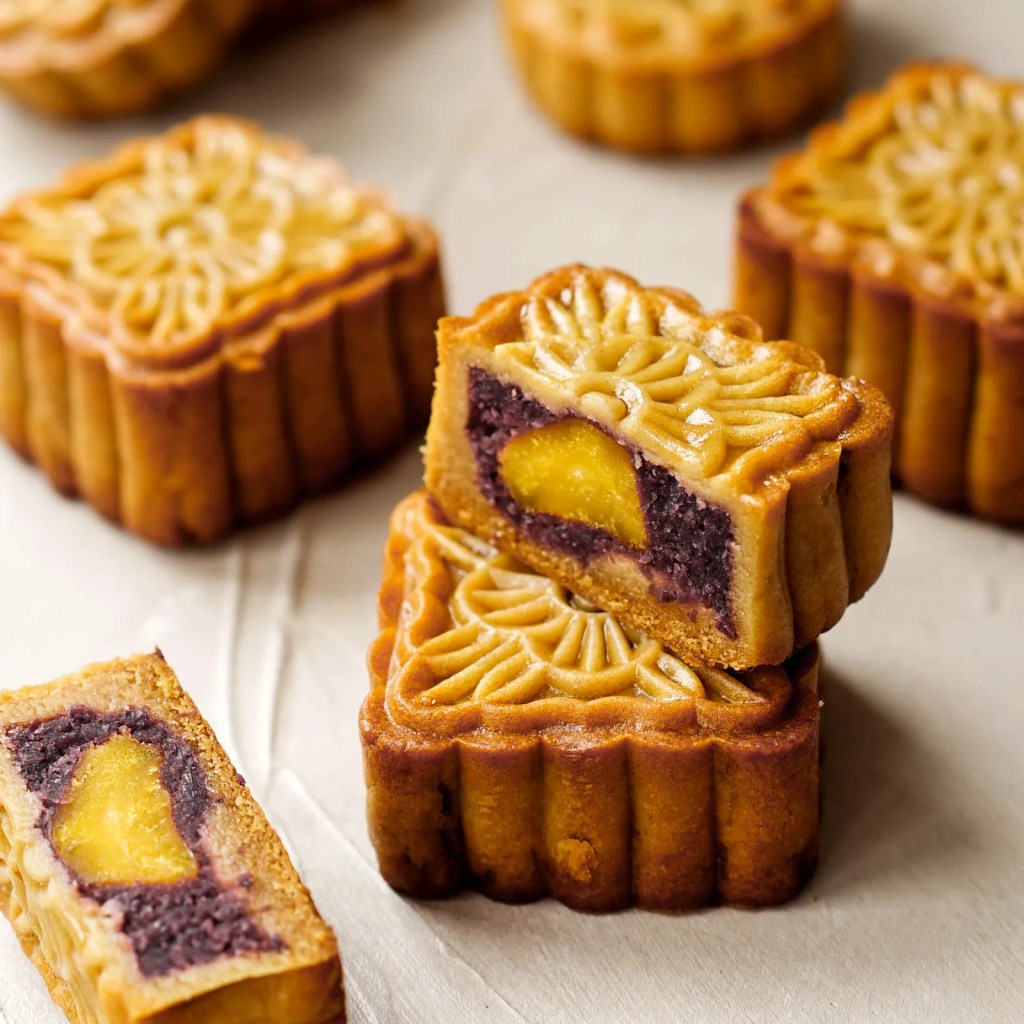 Fried moon cakes stacked in a pile. One is cut in half to show a purple and yellow filling.